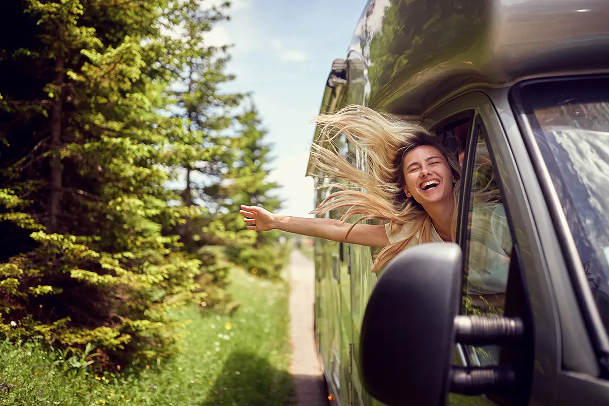 gebrauchtes-wohnmobil-erleben Junge Frau schaut aus dem fahrenden, gebrauchten Wohnmobil und lacht.